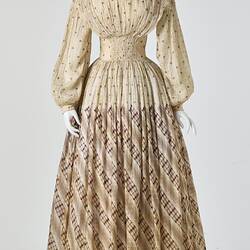 Cream muslin dress, high neck, long sleeves, banded waist, full length patterned gathered skirt.