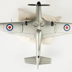 Underside of silver model plane. Blue, white, red roundel on wings. Front has black four blade propeller. Three wheels.