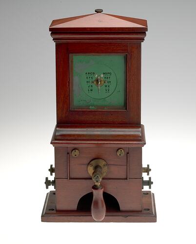 Wooden cabinet with central green section. Wooden handle at base.