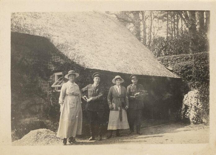 Two woman and two men in front of thatched cottage.