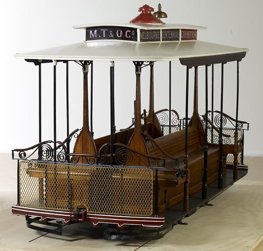 Cable tram model. Open sides with decorative metal frame, wooden bench seats and white roof.