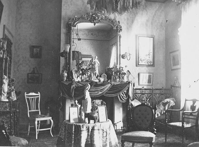 Decorative room with ornate fireplace, pictures on walls, statuettes on tables, luxurious chairs.
