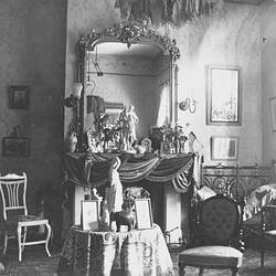 Decorative room with ornate fireplace, pictures on walls, statuettes on tables, luxurious chairs.