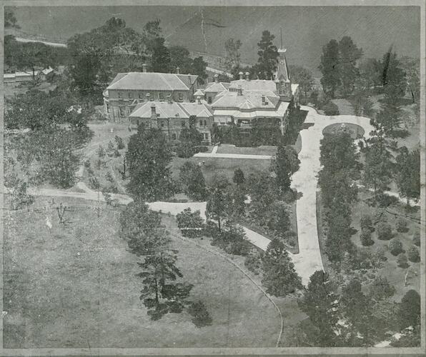 Aerial view of building, includes the driveway and surrounding gardens.