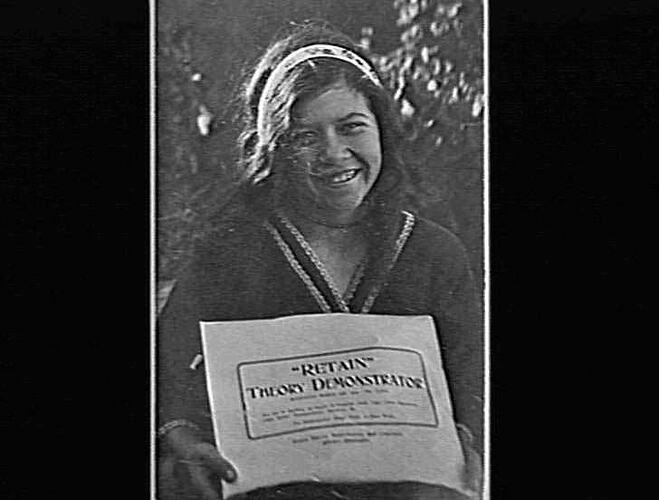 Girl with ribbon in her hair holding a large sheet of paper.