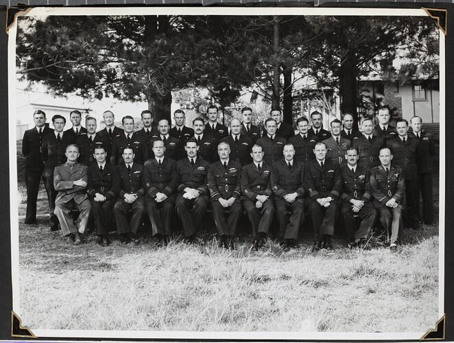 Group portrait of men in military uniform, trees behind.
