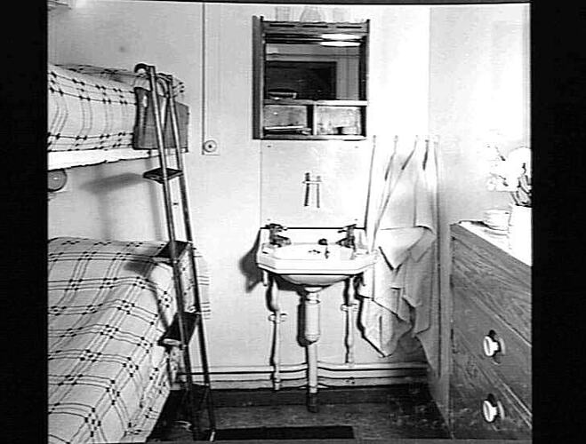 Ship interior. Bunk beds on left. Chest of drawers on right. Handbasin in centre.