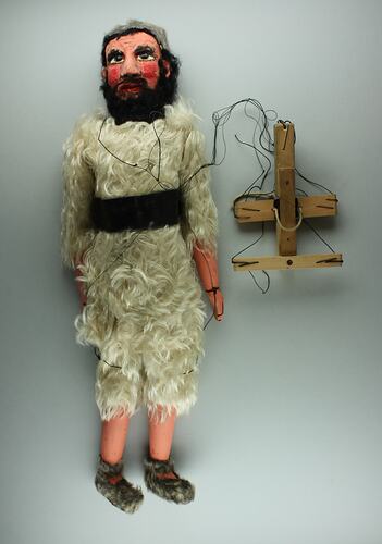 Male marionette in cream fur tunic, brown belt. Black hair and beard. Wooden handle, strings attached.