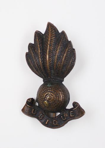 Bronze coloured badge with sphere with flame above and inscribed banner below.