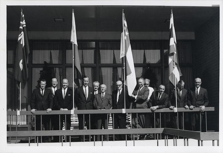 Men in suits on balcony, with flags.