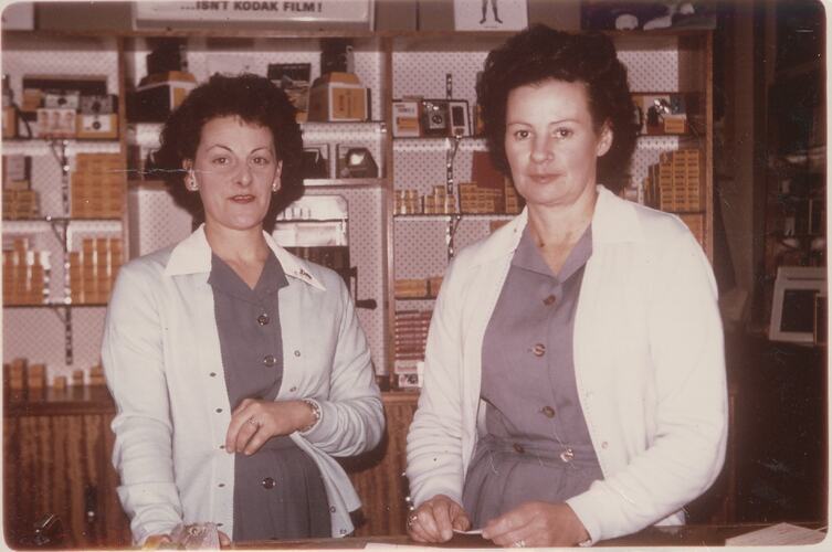 Two women at shop counter in uniform.