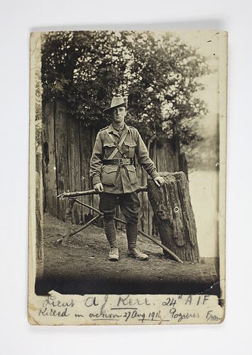 Uniformed soldier with hand on tree trunk.