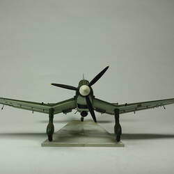 Model aeroplane. Dark green. Black propeller with white tip and black wheels. Front view.