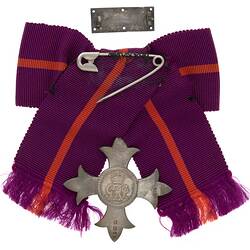 Metal badge with crown attached to purple and red ribbon with safety pin.