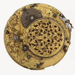 Circular metal watch mechanism with decorative engraving.
