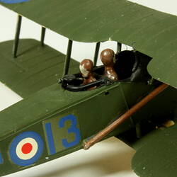 Dark green aeroplane model with red, white, blue circle on side. Detail view of two figurines in cockpit.
