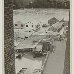 A river in flood and factory buildings partly submerged in the water.
