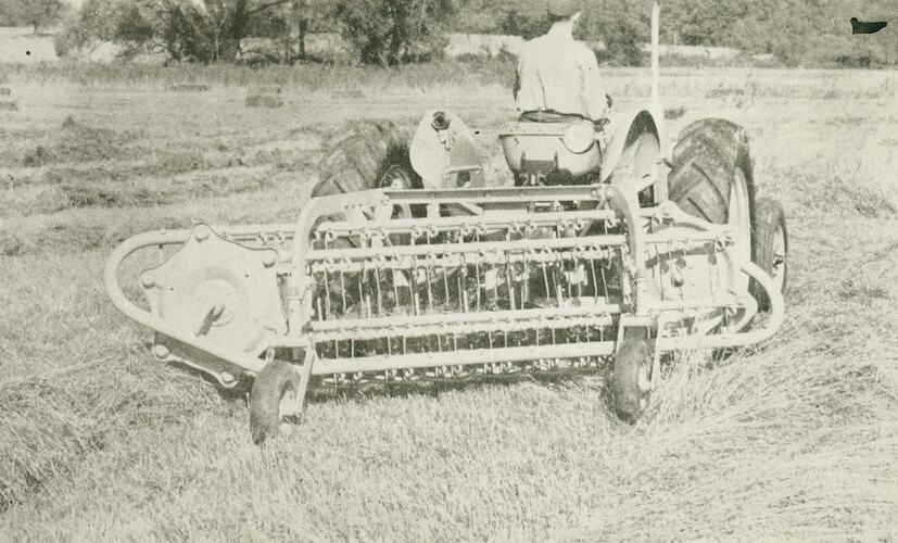 Man driving a tractor with a semi mounted hay rake attached.