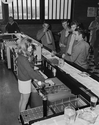 Female hotel worker standing behind bar serving customers.