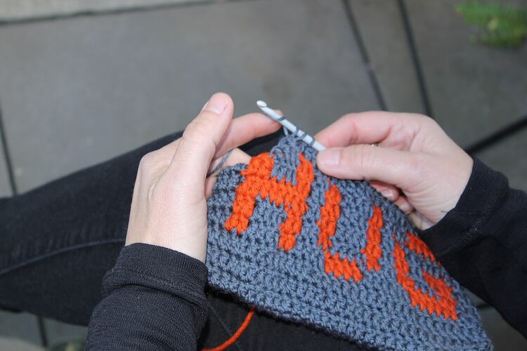 Womans hands crocheting rectangle reading 'HUG'.