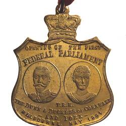 Shield shaped medal with oval portrait of man and woman. Duke and Duchess of Cornwall.