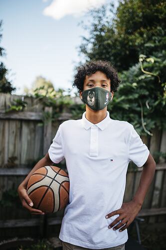 Boy holding basketball wearing a face mask.