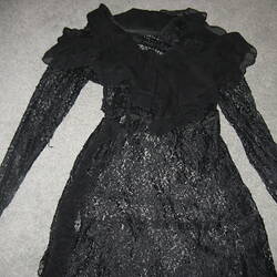 Detail of black lace dress with high frill neck and long sleeves.