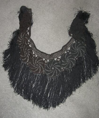 Black crocheted shawl with long black fringe designed in a crescent shape. Crochet work in round circle design
