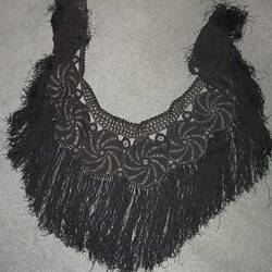 Black crocheted shawl with long black fringe designed in a crescent shape. Crochet work in round circle design