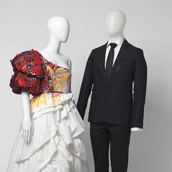 White wedding dress with red shoulder detail and black suit with white shirt, black tie. Detail.
