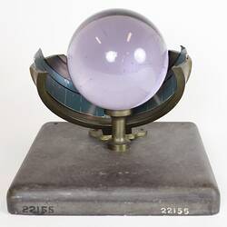 Purple glass sphere sitting on metal frame with square base, front view.