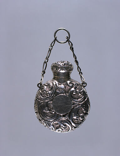 Circular bottle with scrollwork decoration, suspended from chain
