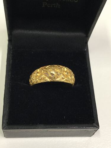 Handcrafted thick gold ring with a central natural gold nugget flanked by floral emblems forming the band.