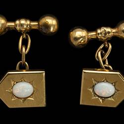 Gold shield shaped cufflinks with central white opals in starcut setting. Chains to barbell togggles.
