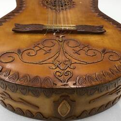 Detail of brown wooden mandolin base with carved decorations on body.