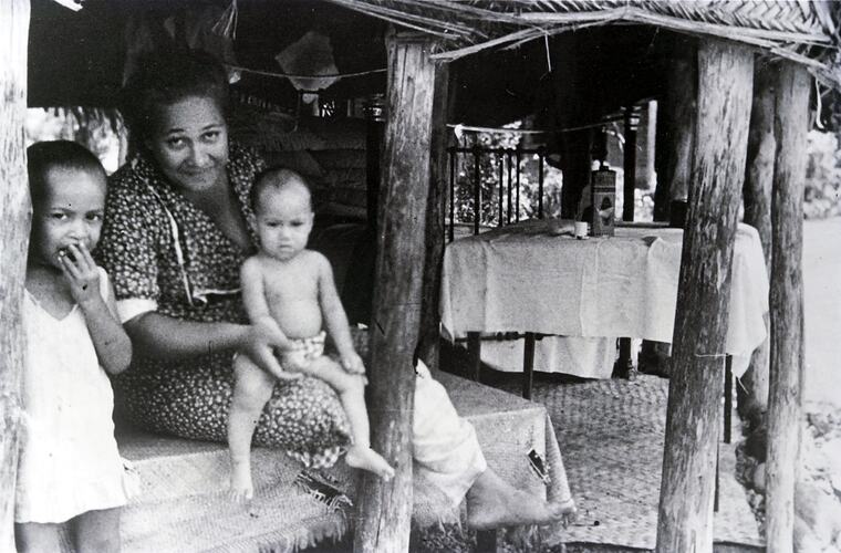 Woman sitting with two children in a hut.