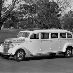 Motor bus with roof rack parked on roadway beside parklands.
