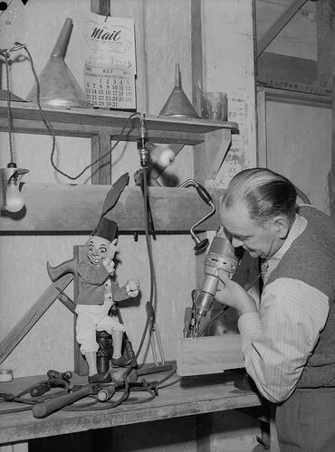 Man operating power drill with puppet nearby.