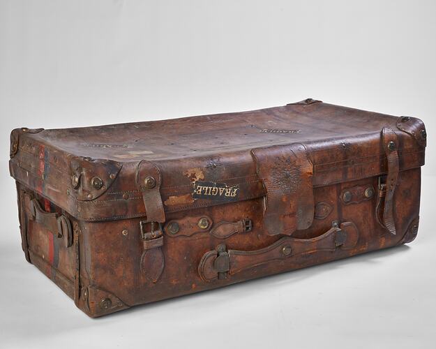 Worn brown leather suitcase with buckles. Fragile label on front.