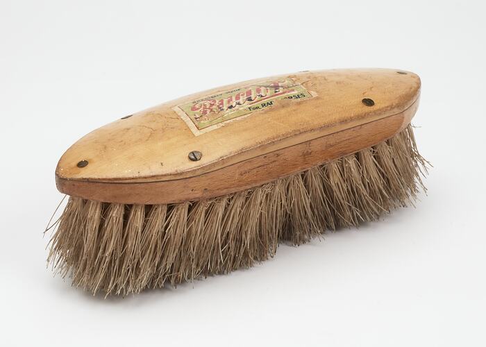 Oval shaped light brown wooden brush with off-white bristles. Colour label on top.