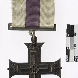 Metal cross with white and purple ribbon.