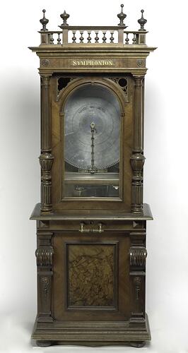 Upright decorative wooden cabinet, a musical box. Contains circular disc.