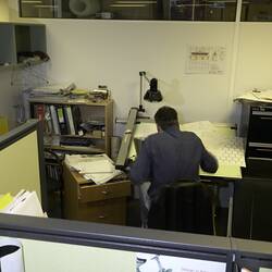 Man sitting at desk in office cubicle. His back is to the camera.