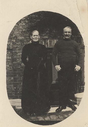 Woman and man in dark clothes standing in front of brick building.