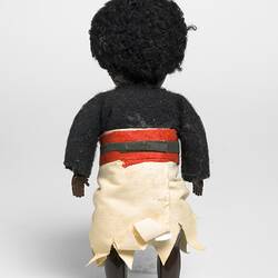 Fijian policeman doll wearing navy long sleeved top, white sulu and red/black belt. Back view.