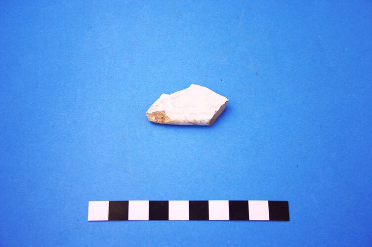 Fragment of white ceramic with moulded scroll pattern.