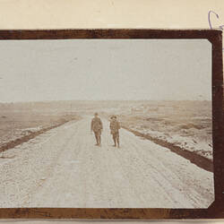 Two servicemen standing on dirt road with flat landscape behind.