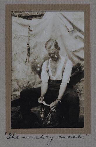 Seated man washing fabric in a bucket.