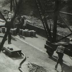 Group of people standing by wooden crates on left, man carrying crate on right.