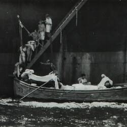People walking down a staircase attached to a ship and into a lifeboat in the water.